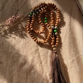 Japamala de semillas de rudraksha ligeramente aplanadas con una gema de agata verde y cuentas de cristal de murano verde con detalles dorados y borla de hillo color chocolate