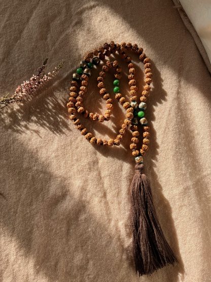 Japamala de semillas de rudraksha ligeramente aplanadas con una gema de agata verde y cuentas de cristal de murano verde con detalles dorados y borla de hillo color chocolate